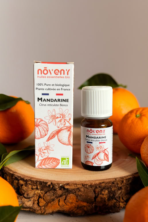 Boîte et flacon de produit sur une tranche de bois entourés de mandarines et de feuilles vertes.
