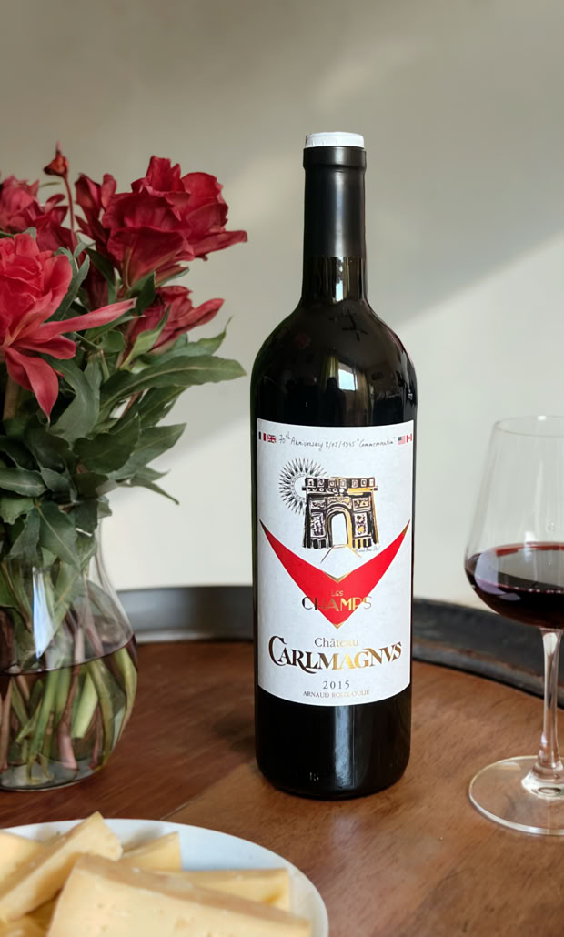 Bouteille de vin rouge sur une table en bois avec un verre de vin à côté, un bouquet de fleurs rouges et une assiette de fromage.
